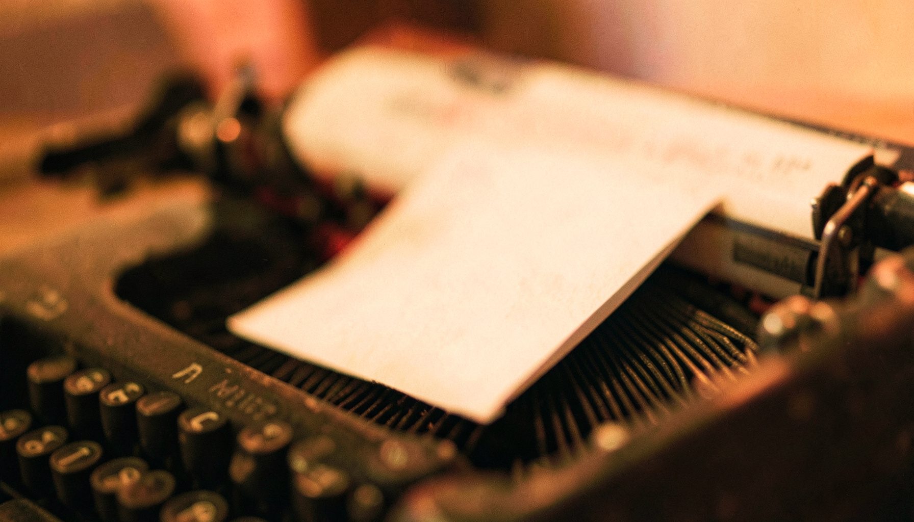 Soft-focus close-up of a vintage typewriter with a sheet of paper, warm cream and muted rose tones, shallow depth of field
