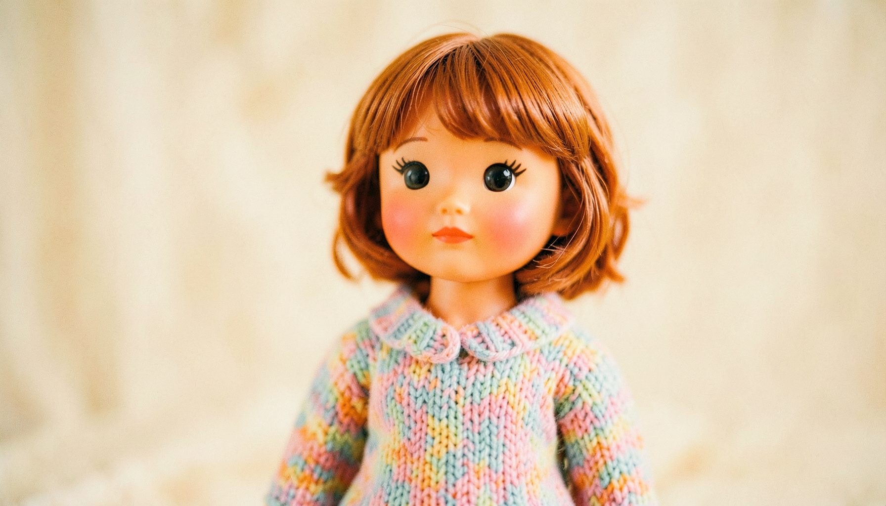 A Blythe doll wearing a hand-knit pastel sweater against a soft cream backdrop, shallow depth of field